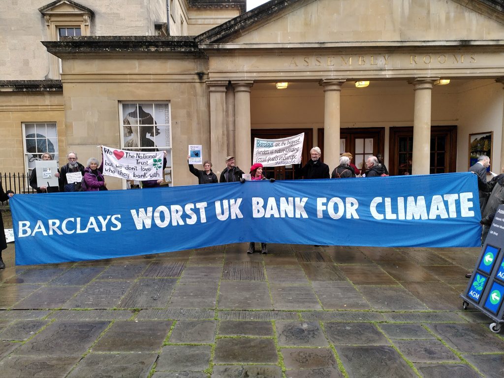 protesters hold banner outside national trust agm saying barclays worst uk bank for climate