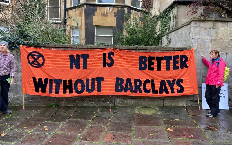 Protesters hold up banner outside National Trust AGM saying better without barclays