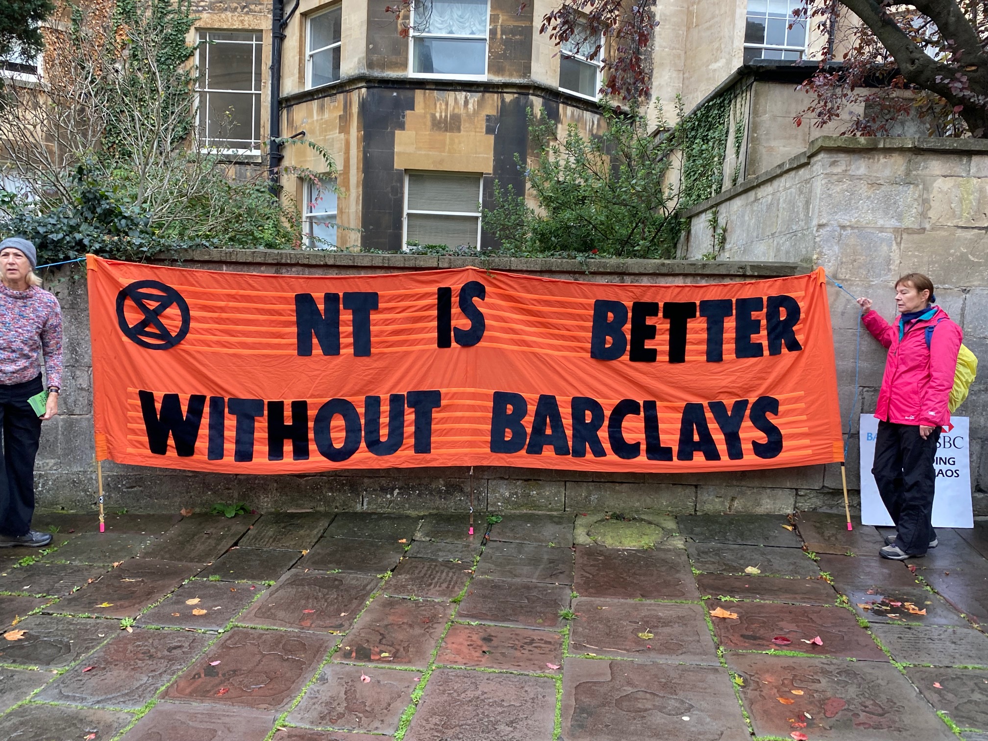 Protesters hold up banner outside National Trust AGM saying better without barclays